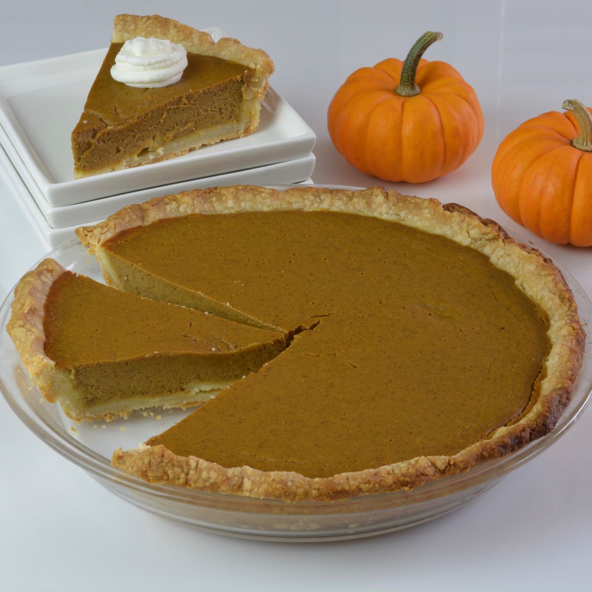 A whole gluten free Pumpkin Pie with one piece placed on a plate and 2 mini pumpkins beside it.
