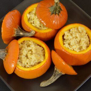 Top down view of sugar pumpkins filled with pumpkin risotto served on a black plate.
