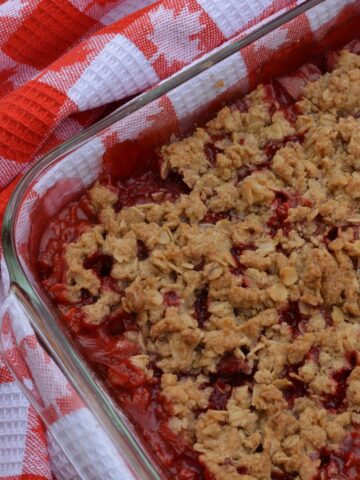 A pan of Rhubarb Strawberry Crisp surrounded by a tea towel with a maple leaf pattern.