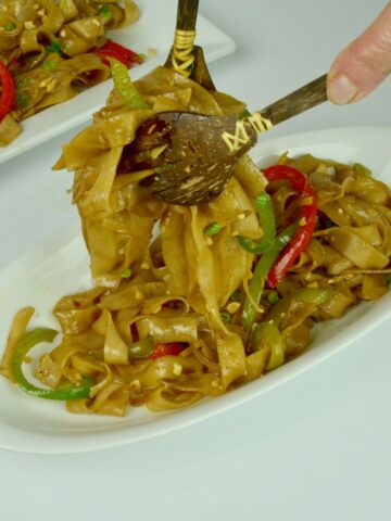 Close up of cooked rice noodles with red and green pepper garnished with chopped peanuts.