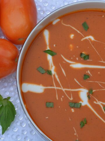 Top down view of homemade Roasted Tomato Soup wth a random spattering of yogurt, sprinkled with fresh basil.