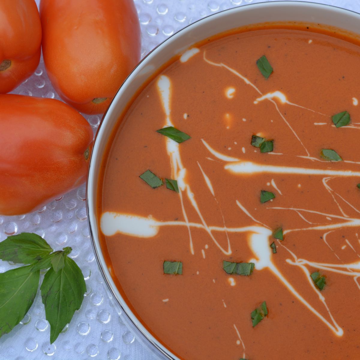 Top down view of homemade Roasted Tomato Soup wth a random spattering of yogurt, sprinkled with fresh basil.