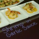 Three small plates each with three shrimp in garlic sauce to be served.