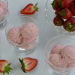 Dishes of Strawberry Cheesecake Ice Cream surrounded by fresh strawberries.