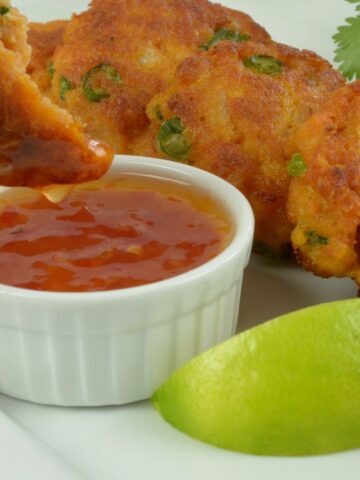 A platter of Thai Fish Cakes and someone dipping one into the sweet chile sauce.