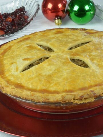 A whole tourtiere on a red platter with a dish of cranberry chutney and a few Christmas balls.