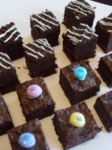 A plate of cut Gluten Free Chocolate Truffle Brownies decorated with melted white chocolate and m&m's.