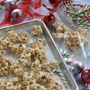 A pan with clumps of White Chocolate Candy Cane Popcorn beside the gift bags, candy canes and ribbon ready for gift wrapping.