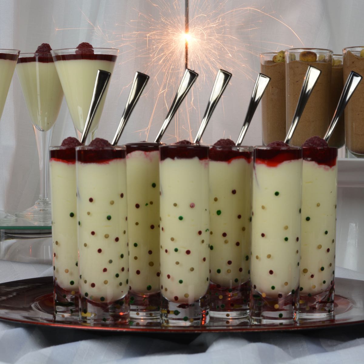 A tray of White Chocolate Mousse shots with raspberry sauce and a raspberry on top.