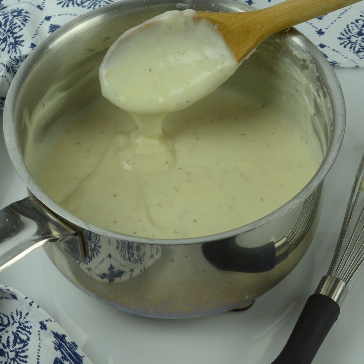 A pot of white sauce and a wooden spoon showing how thick it is.
