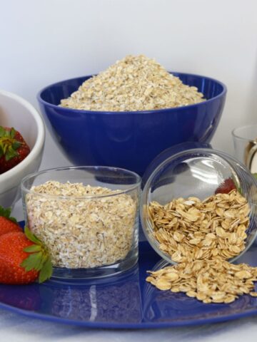 Dishes showing gluten free whole oats vs quick oats on a blue plate surrounded by strawberries.