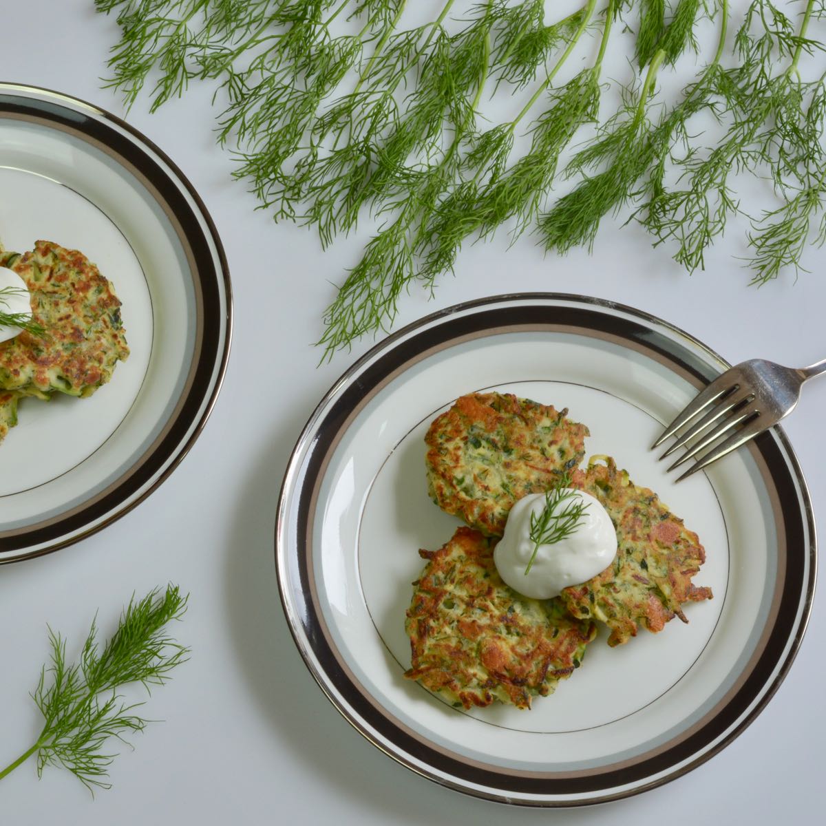 Two plates serving up Pan Fried Zucchini Fritters topped with sour cream and garnished with dill.