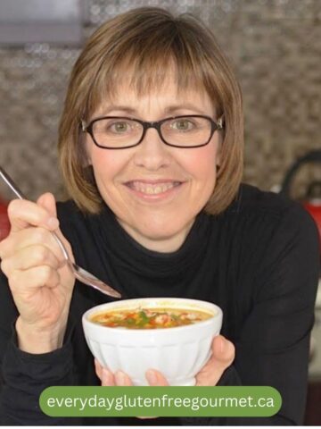 Cinde in her kitchen holding a bowl of soup with a spoon in hand.