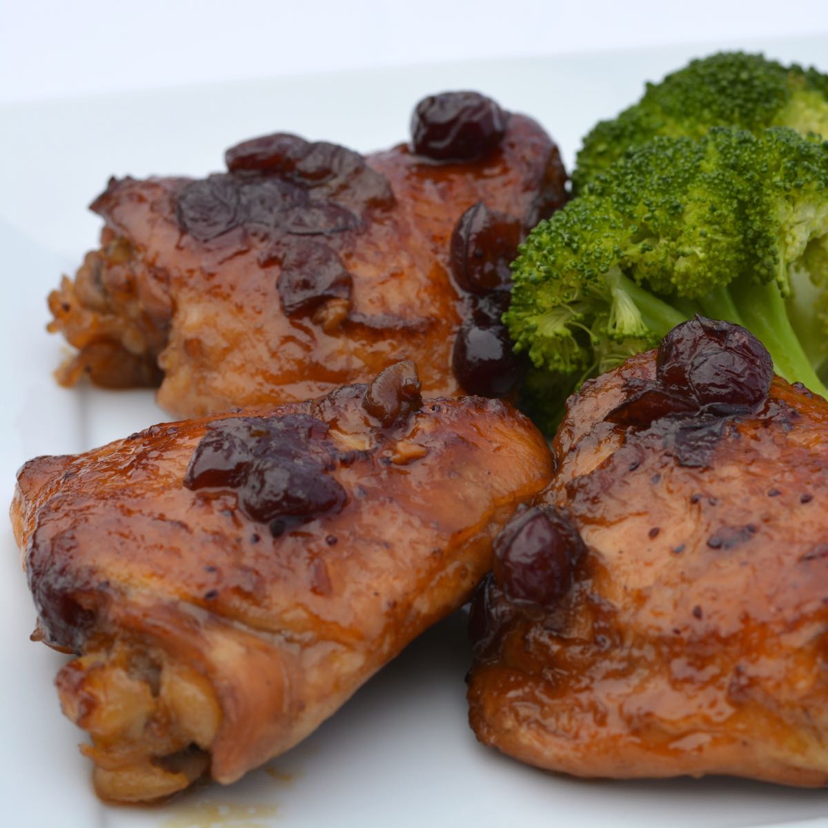 Three thigh pieces of gluten free Cranberry Orange Chicken and steamed broccoli.