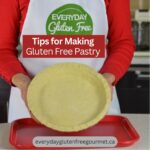 Cinde wearing her apron and holding a pie plate with raw pastry in it.