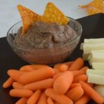 A dish of Black Bean Dip with baby carrots and jicama sticks.