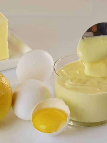 Butter, eggs and a lemon beside a dish of Blender Hollandaise Sauce.