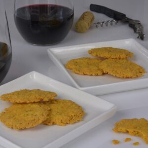Two plates with a few Cheddar Cheese Wafers beside glasses of red wine.