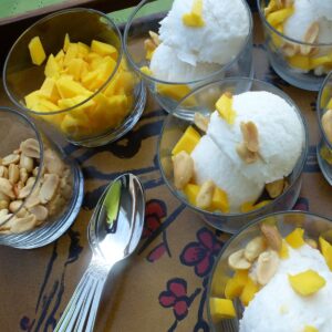 Close up of small glass dishes with coconut ice cream topped with mango and peanuts.
