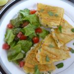 A plate with crab quesadillas topped with chipotle mayo and a tossed salad on half the plate.