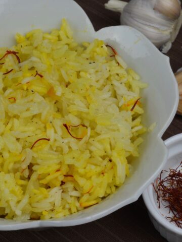 A bowl of fragrant Saffron Rice beside whole garlic cloves and saffron threads.
