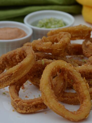 A plate of gluten free calamari with dishes of ancho chile mayo and lime salt on the side.