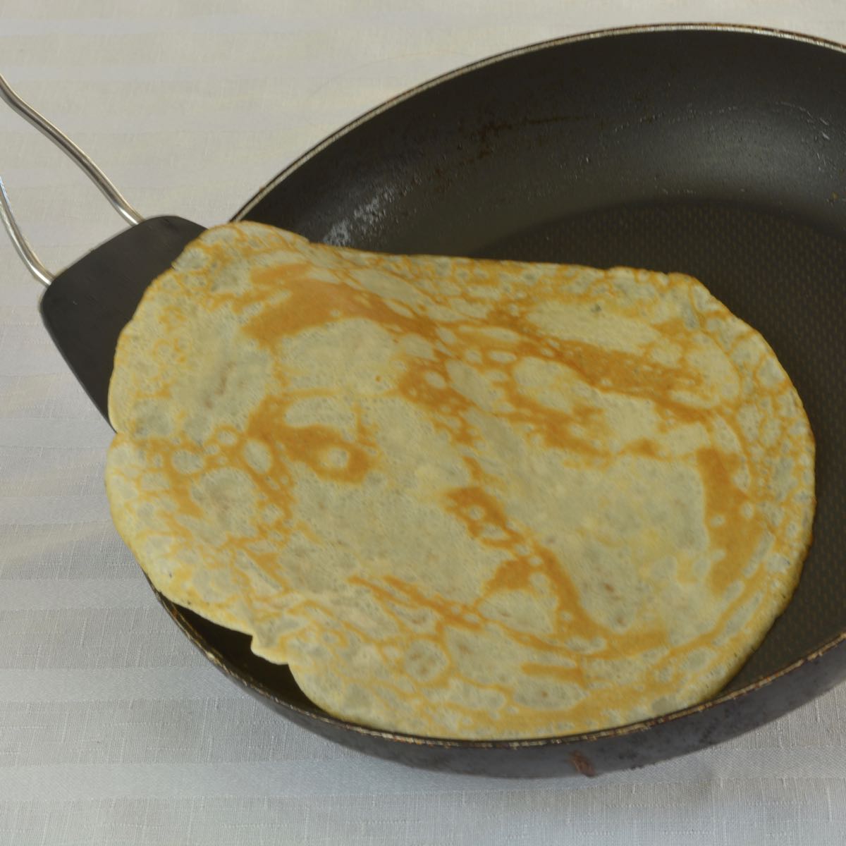 A frying pan with a flipper and a crepe that has just been turned.