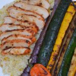 A platter with slices of grilled Achiote Chicken, summer squash and red onion.