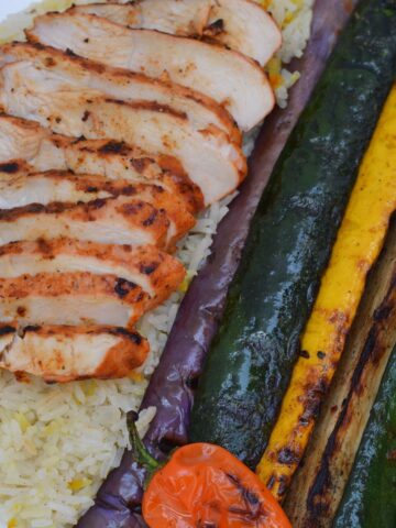 A platter with slices of grilled Achiote Chicken, summer squash and red onion.