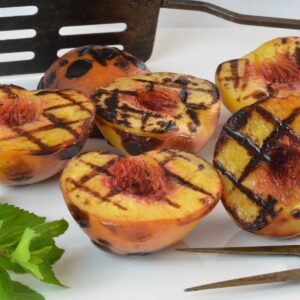 A plate of Grilled Peaches with a barbecue flipper behind it.