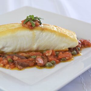 A plate of Halibut Puttanesca on top of a fresh tomato sauce with capers.
