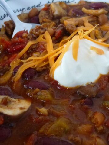 A bowl of Homemade Chili topped with sour cream and sprinkled with shredded cheddar cheese.