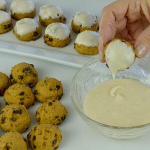 A hand dipping Pumpkin Spice Cookies into a small bowl of icing.