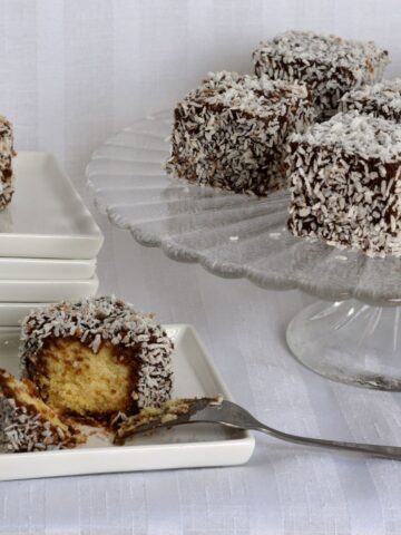 A pedestal tray with squares of gluten free lamingtons, with small plates beside it and one lamington cut into with a fork.