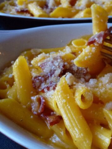 A fork grabbing some macaroni and cheese with bits of bacon from a dish.