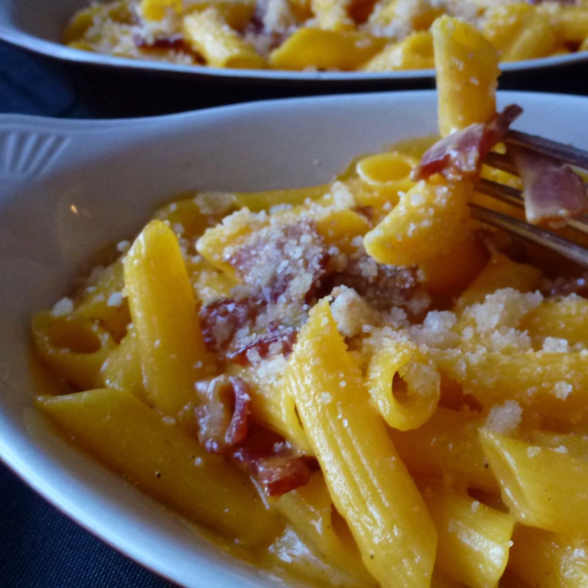 A fork grabbing some macaroni and cheese with bits of bacon from a dish.