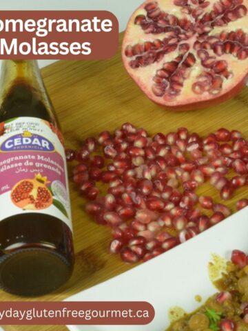 A bottle of store bought pomegranate molasses beside a cut pomegranate and the seeds (actually called arils) beside it.