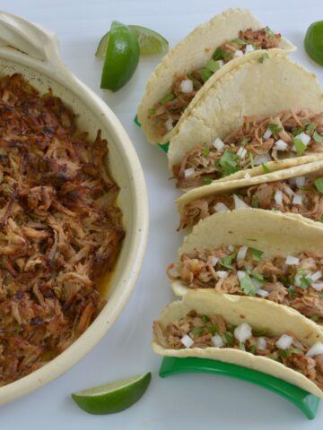 A platter of Mexican Pork Carnitas surrounded by tacos filled with the pork.