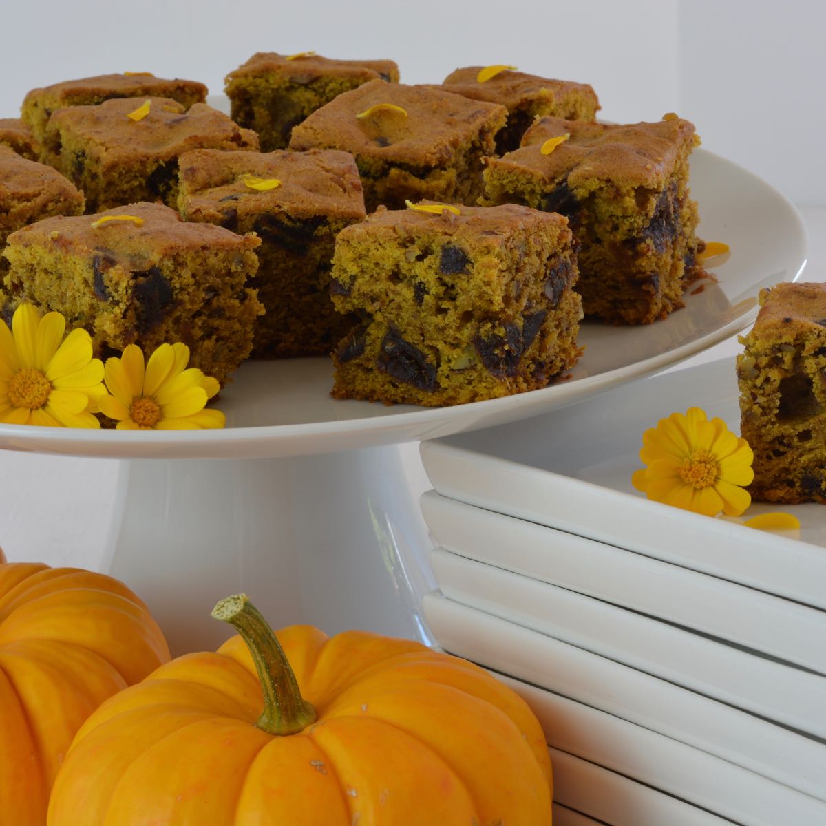 Cut pieces of Pumpkin Date Cake on a pedestal tray garnished with edible flowers and surrounded my mini pumpkins.