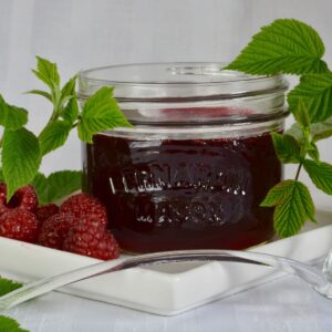 A Mason jar filled with Raspberry Sauce and surrounded by a raspberry branch and some fresh berries.ct to pour over ice cream, brownies or grilled peaches.