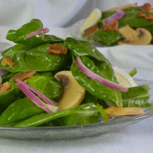 A wooden bowl and tongs with Spinach Salad with Hard Boiled Eggs and bacon.