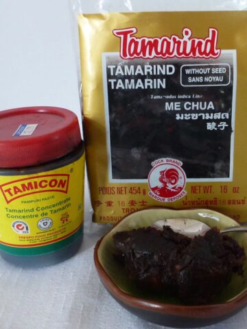 A tub of Tamarind concentrate beside a package of tamarind paste, with a small dish in front showing the paste.