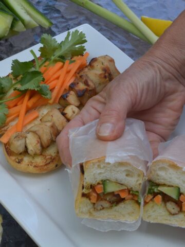 A Vietnamese Lemongrass Chicken Sub, wrapped in wax paper and cut in half showing the carrot, cucumber and cilantro filling.