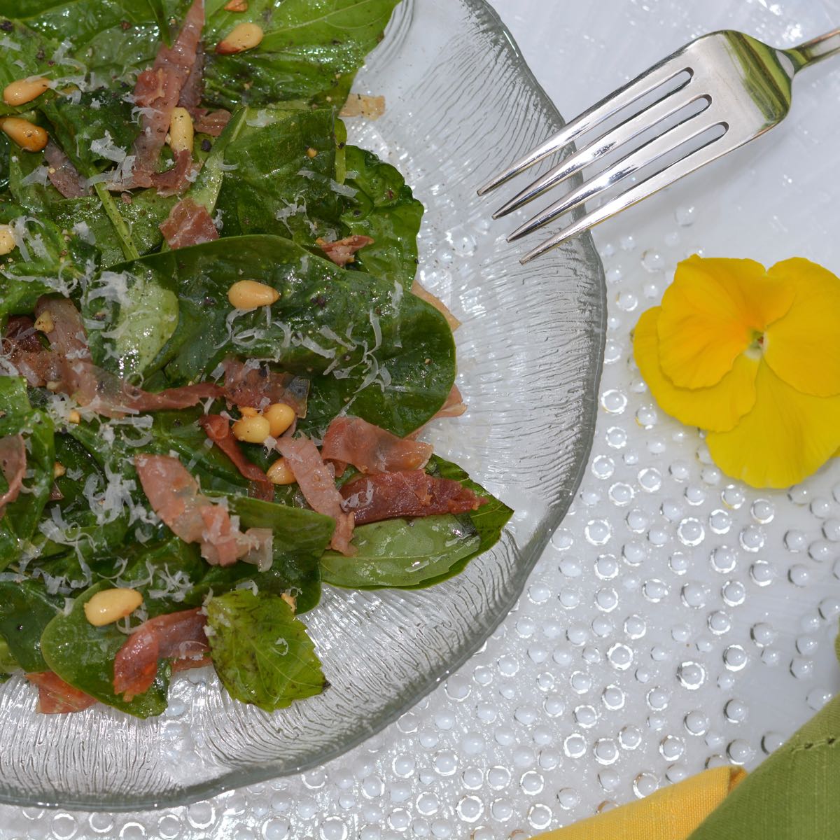 A Warm Spinach Basil Salad on a plate with pine nuts and frizzled prosciutto.