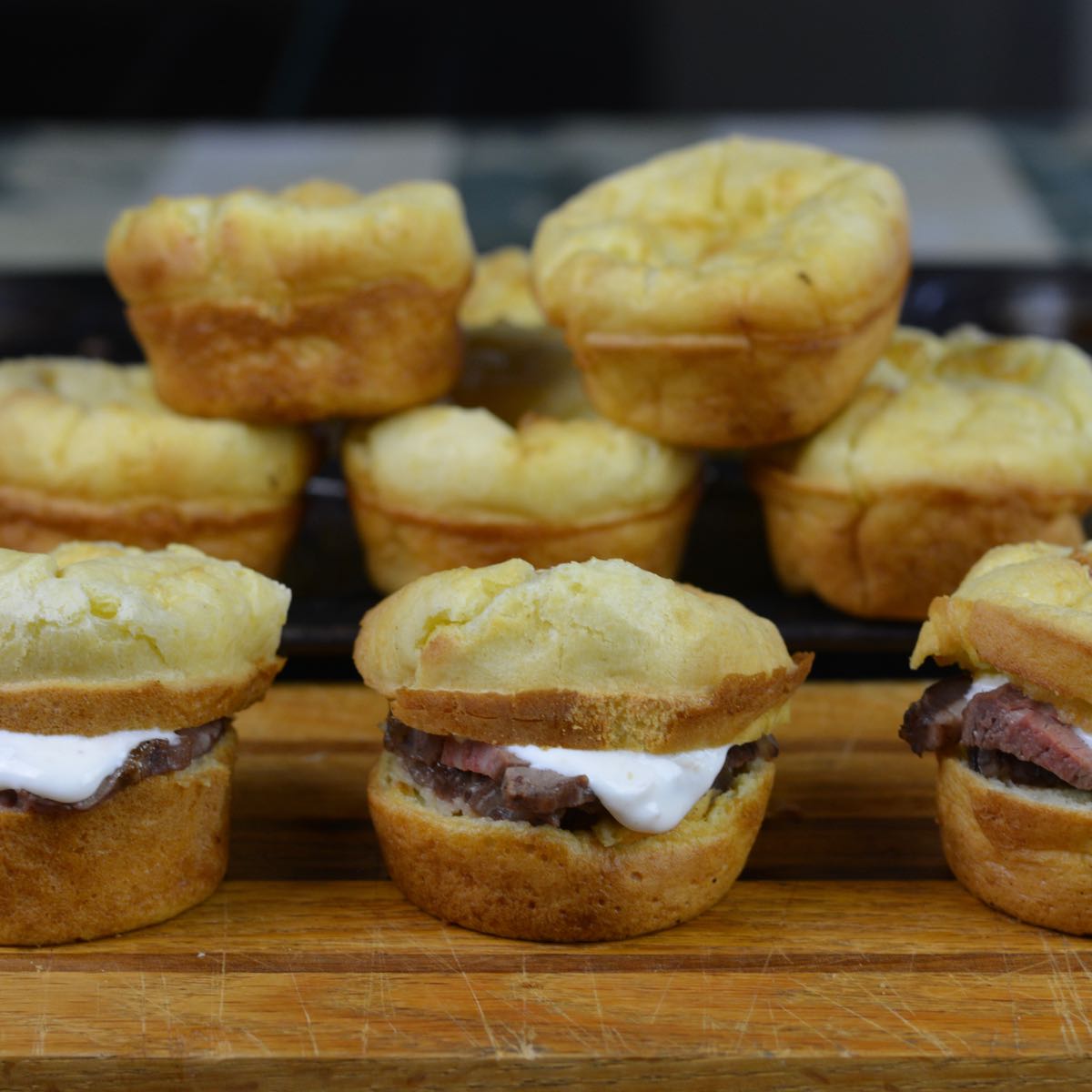 A board with three gluten free Yorkshire Pudding Sliders showing a piece of roast beef with a bit of horseradish cream sauce.