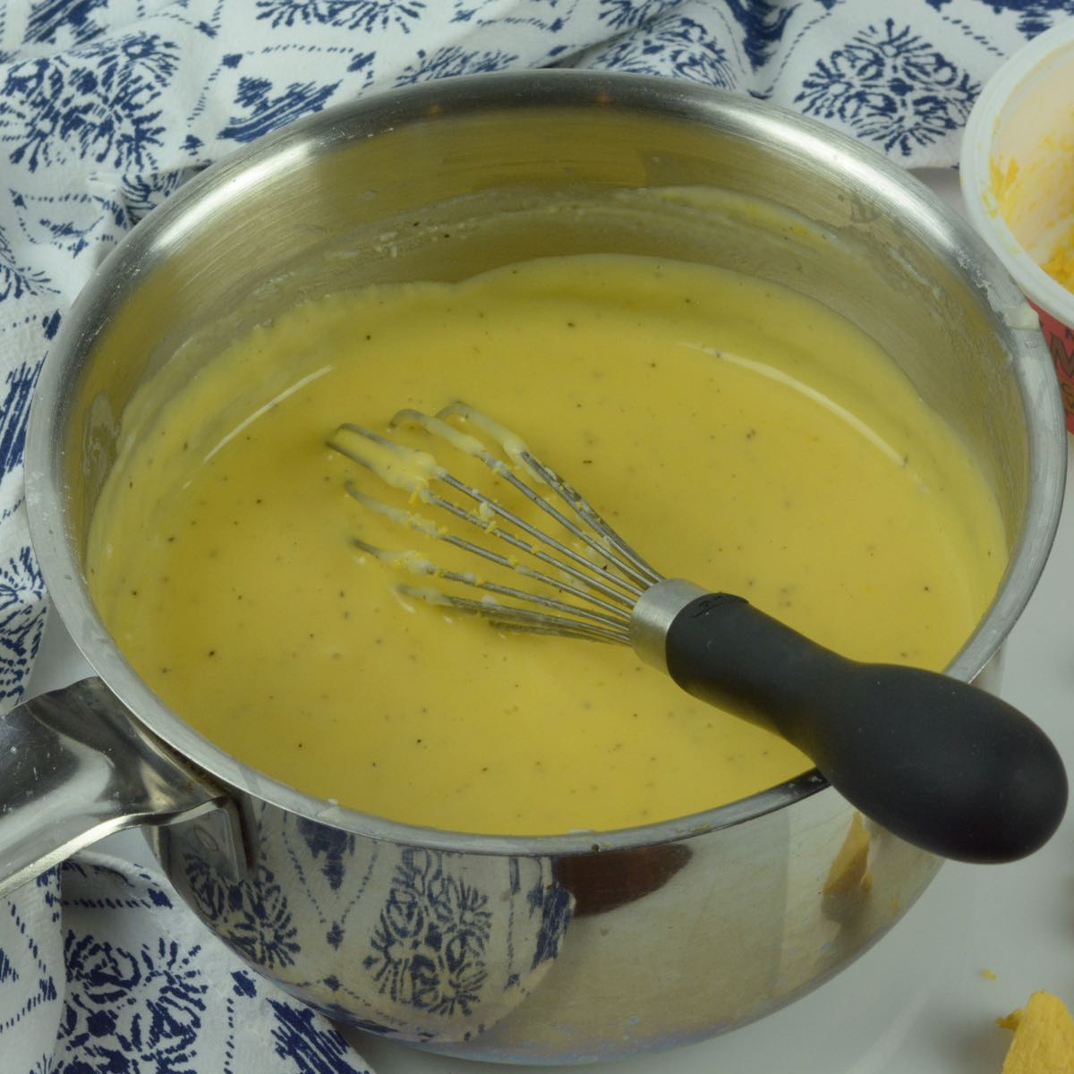 A pot of smooth cheese sauce with a whisk in it.