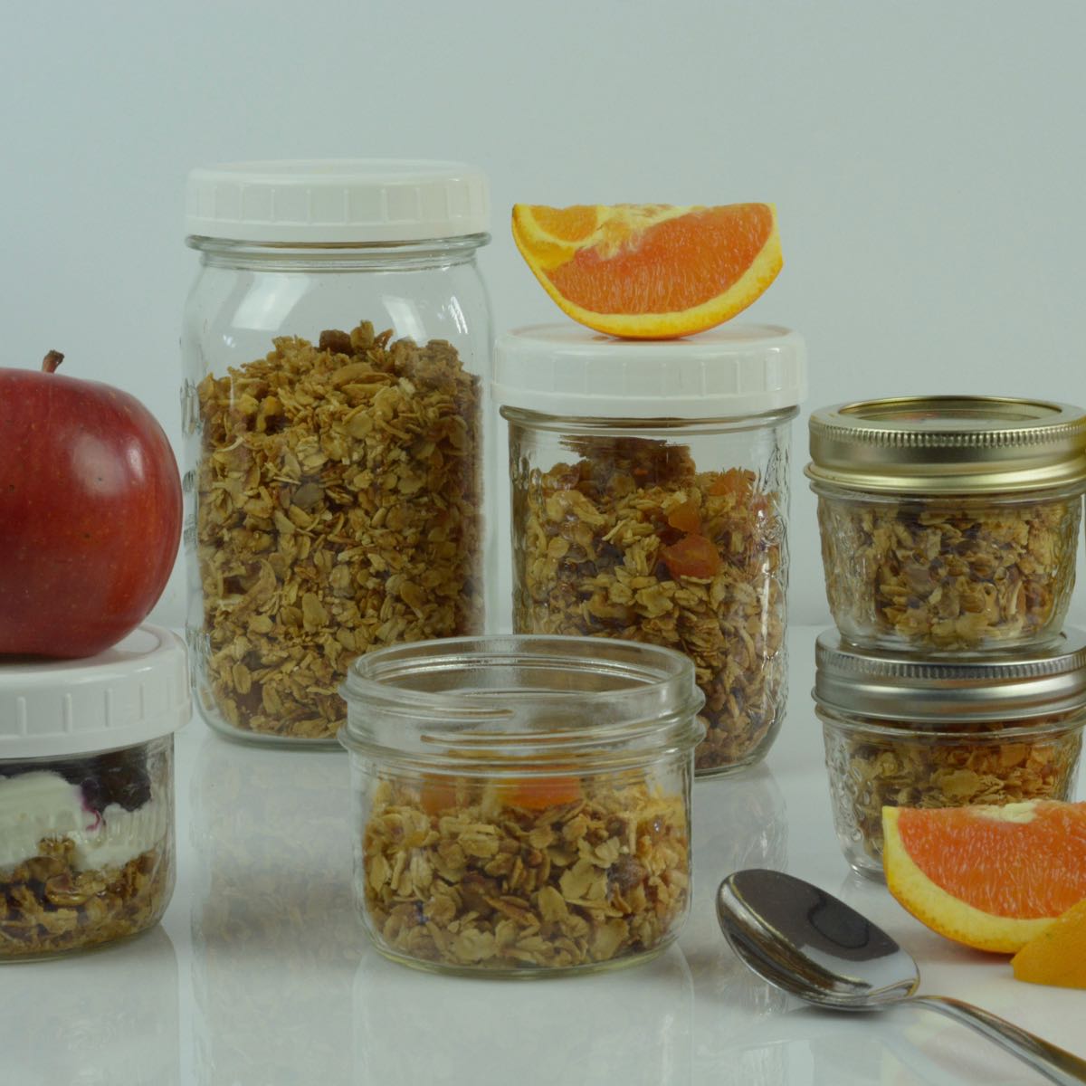 Jars filled with Gluten Free Pistachio Apricot Granola topped with apples and oranges.