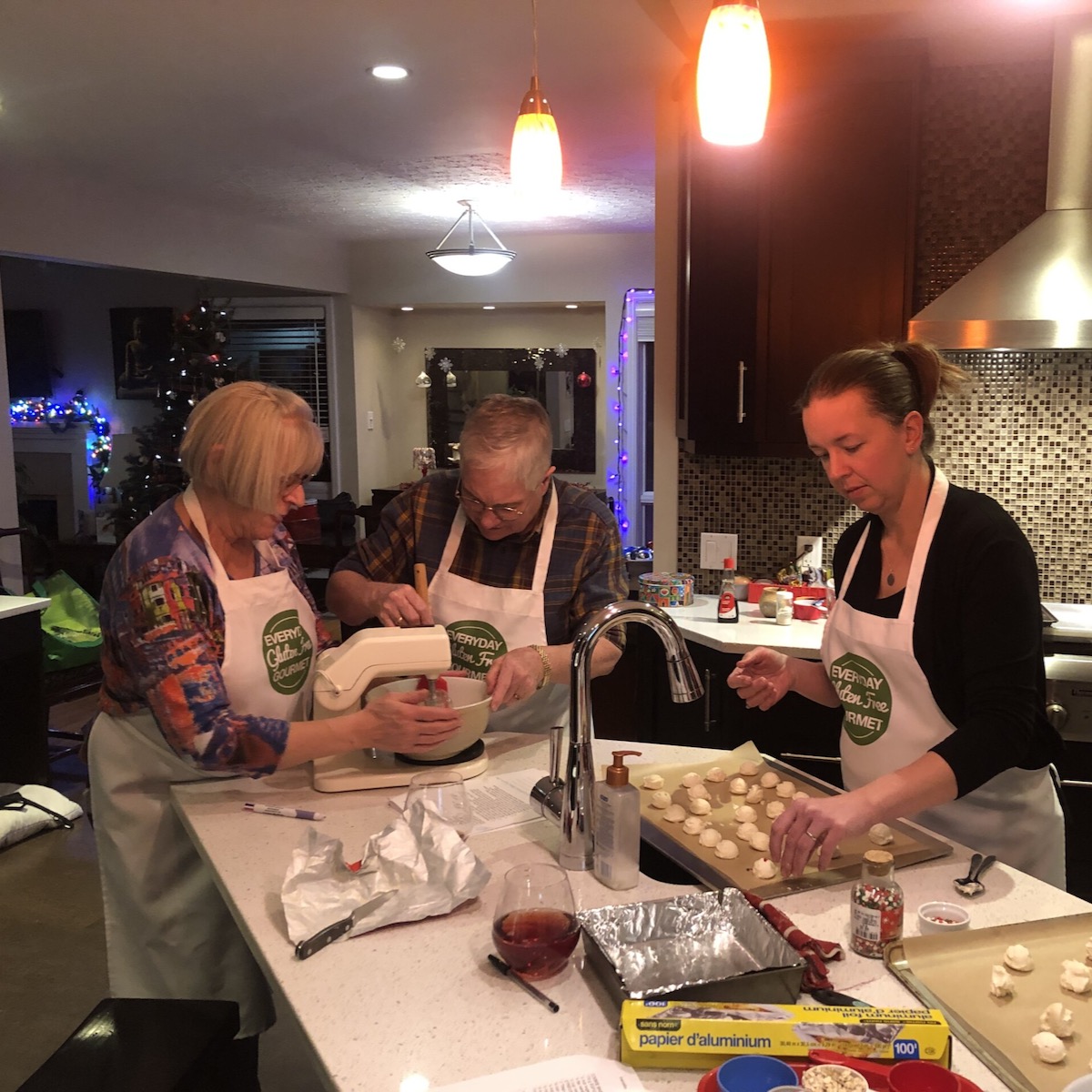 Three ladies in the kitchen, two at the stand mixer and one adding cherries to the shortbread.
