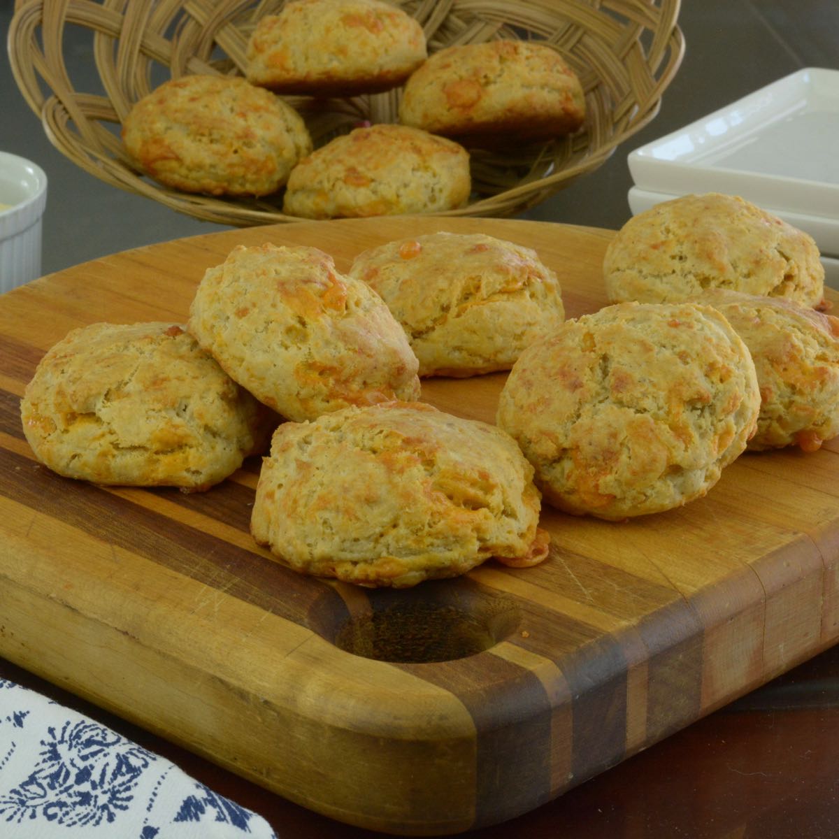 Gluten free Cheese Biscuits served on a board with a basket behind them holding more.