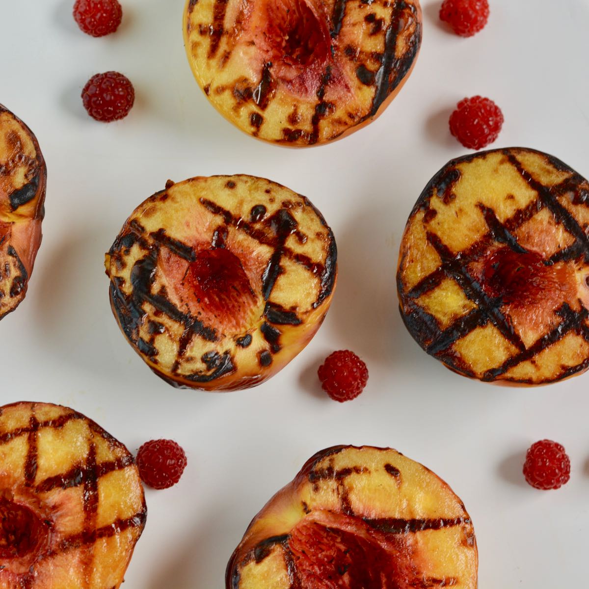 A plate with Grilled Peaches and raspberries.